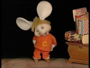 Personaggio animato con orecchie da coniglio e costume arancione.